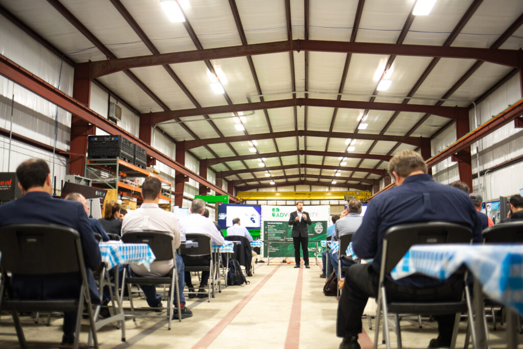 People sit in chairs on both sides of an aisle as a speaker stands in the background